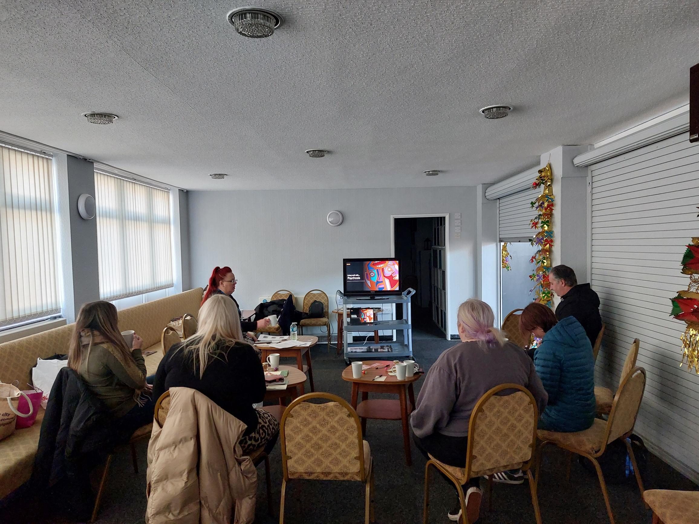 Wellbeing College students and facilitators sitting down looking at Living well with psychosis slide set on screen