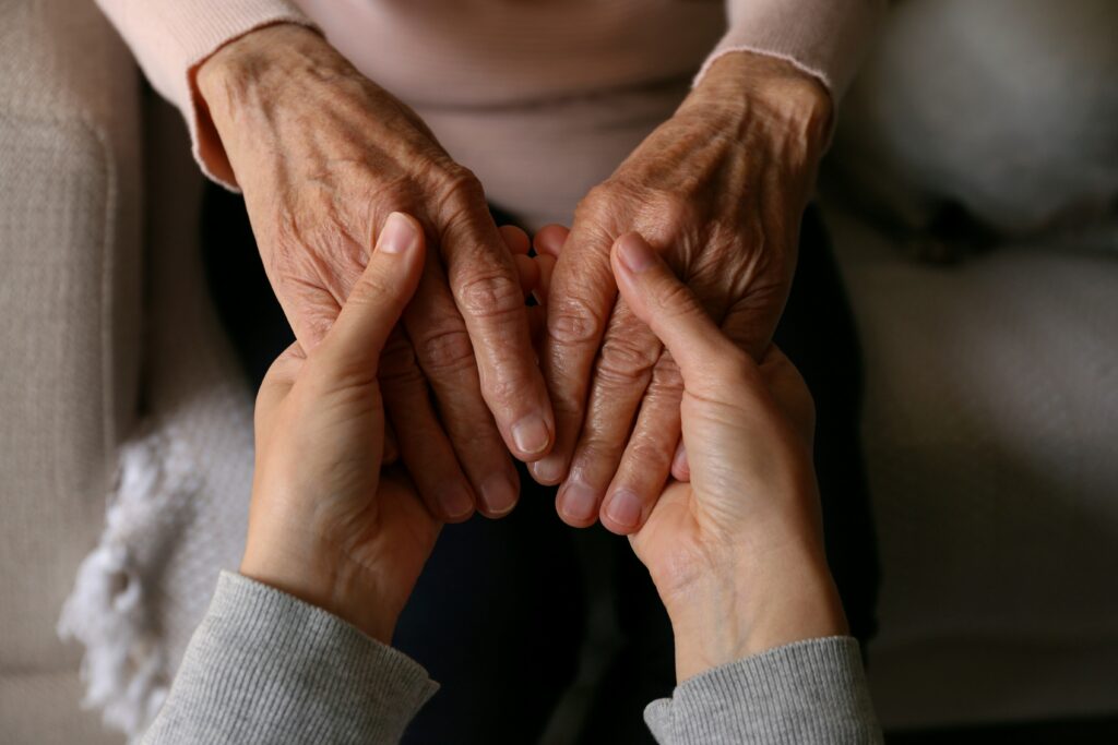 Cropped shot of elderly woman and female geriatric social worker holding hands. Women of different age comforting each other.-