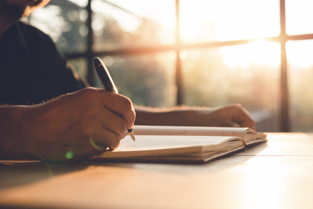 Hand holding pen and writing note on wood table.