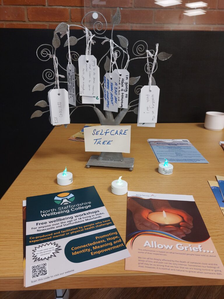 Small tree with self-care messages on tags, candles and flyers for Dove bereavement service and Wellbeing College