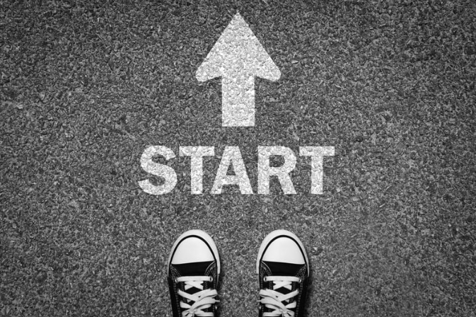 Black converse-type shoes on pavement with word Start and arrow in white