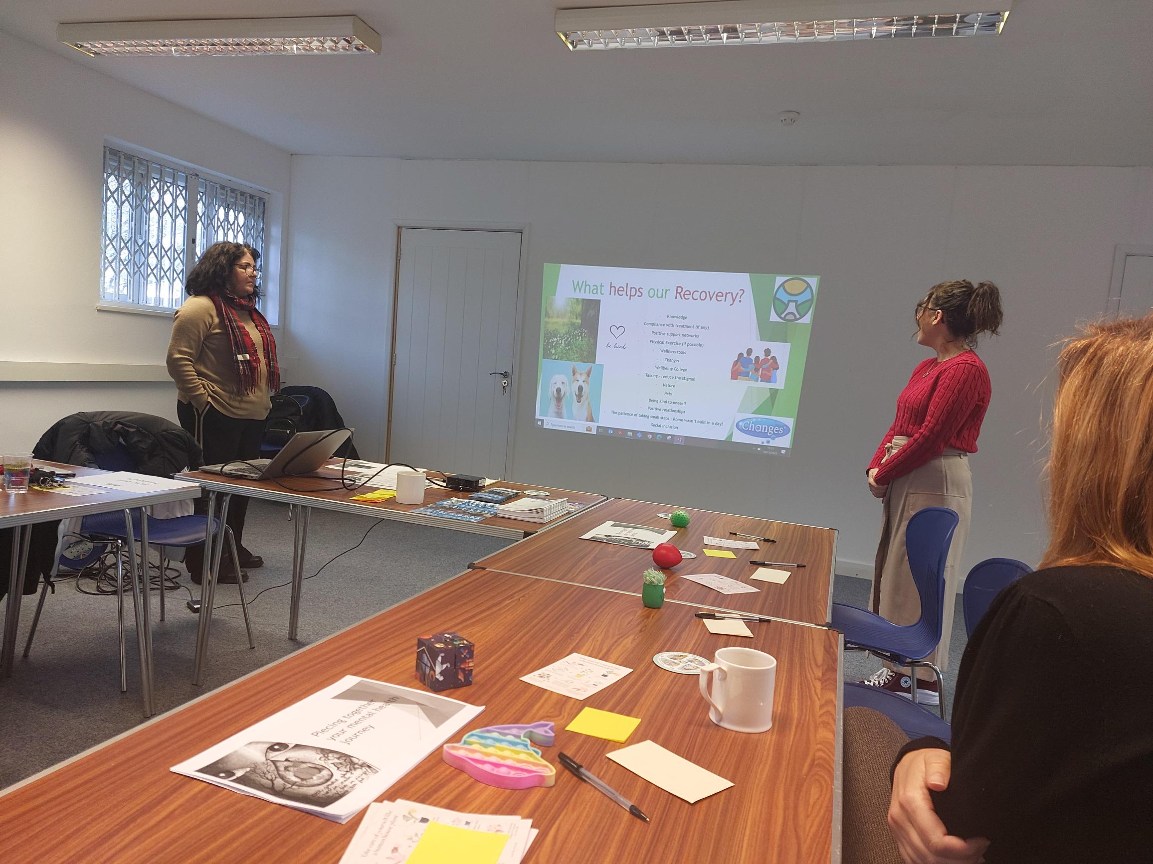 Two female facilitators delivering workshop standing up by PowerPoint presentation on wall